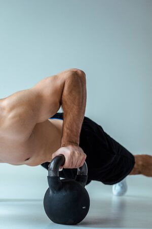 partial view of sexy muscular bodybuilder with bare torso doing push ups with kettlebell on greyの写真素材