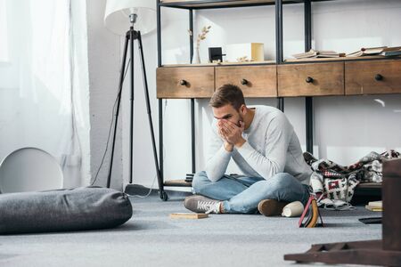handsome and shocked man obscuring face in robbed apartment