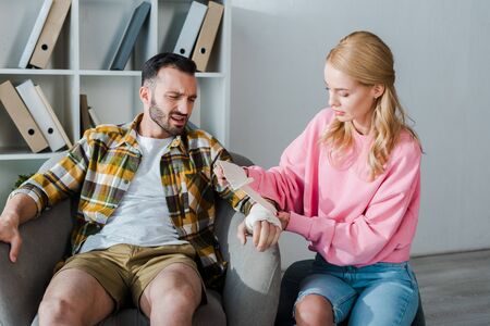 caring woman putting bandage on injured hand of bearded manの写真素材