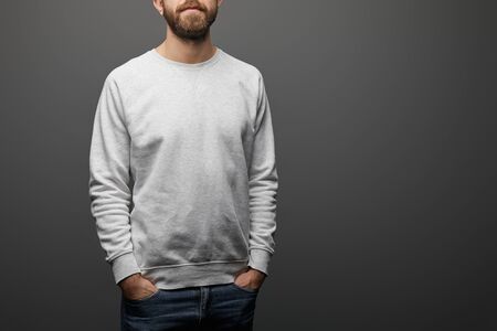 cropped view of bearded man with hands in pockets in blank basic grey sweatshirt on black backgroundの写真素材