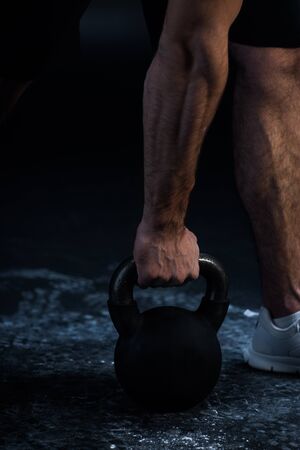 cropped view of muscular bodybuilder excising with kettlebell on blackの写真素材