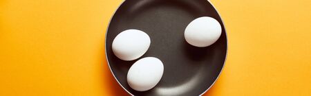 top view of raw chicken eggs in frying pan on orange background, panoramic shotの写真素材
