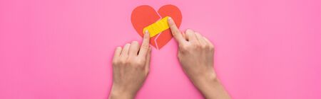cropped view of woman putting patch on broken paper heart isolated on pink background, panoramic...