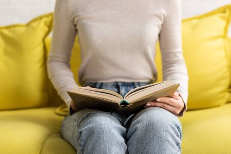 Cropped view of woman reading book on couch at homeの写真素材