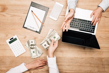 Top view of business partners with dollar banknotes, laptop and calculator on table