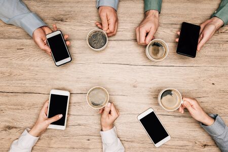 Top view of business people drinking coffee and using smartphones at wooden table, cropped viewの写真素材
