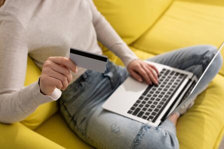 Cropped view of woman holding credit card and using laptop on couchの写真素材