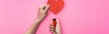 cropped view of woman lighting up empty red paper heart with lighter isolated on pink, panoramic shotの写真素材