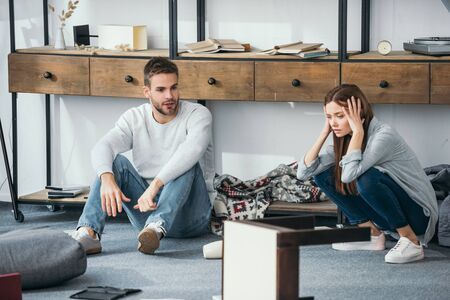 sad woman and handsome man sitting on floor in robbed apartmentの写真素材