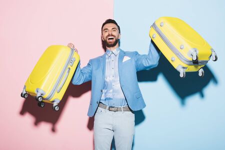 smiling man holding travel bags on pink and blue backgroundの写真素材