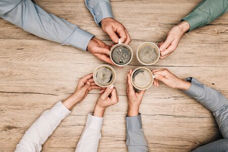 Top view of colleagues drinking coffee at wooden table, cropped view