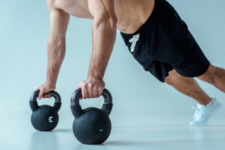 partial view of sexy muscular bodybuilder with bare torso doing push ups with kettlebells on greyの写真素材
