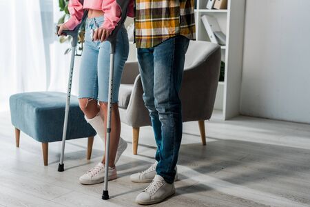 cropped view of man standing with injured woman holding crutches at homeの写真素材