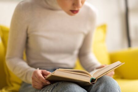 Cropped view of woman reading book on couch