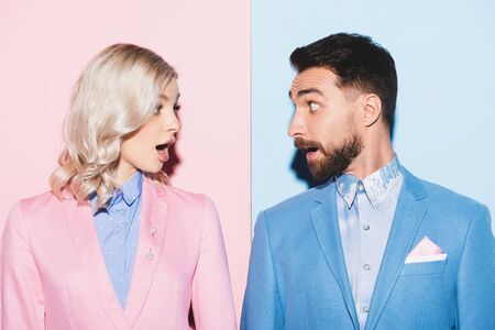 shocked woman and handsome man looking at each other on pink and blue backgroundの写真素材