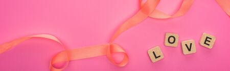 top view of curved ribbon and wooden blocks with love lettering isolated on pink, panoramic shotの写真素材