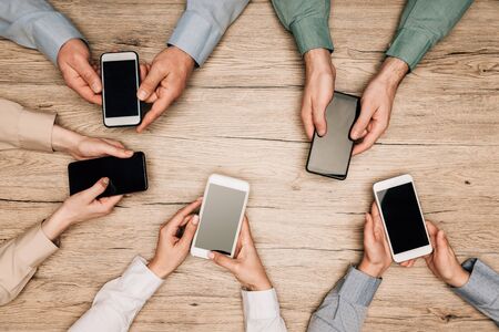 Top view of business people holding smartphones with blank screens on table, cropped viewの写真素材