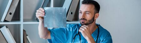 panoramic shot of handsome orthopedist looking at x-ray
