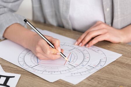 Cropped view of astrologer drawing natal chart on wooden tableの写真素材