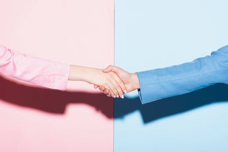 cropped view of woman and man shaking hands on pink and blue backgroundの写真素材