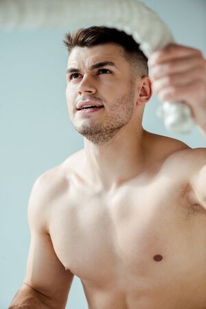 sexy muscular bodybuilder with bare torso exercising with battle rope isolated on greyの写真素材