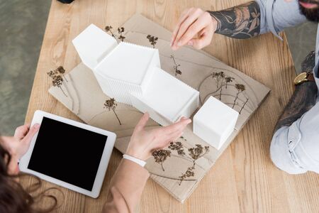 cropped view of virtual reality architects sitting at table with model of house