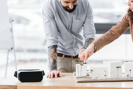 cropped view of virtual reality architects pointing with finger at model of house