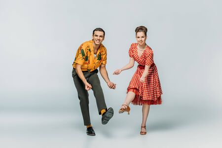 cheerful dancers looking at camera while dancing boogie-woogie on grey backgroundの写真素材
