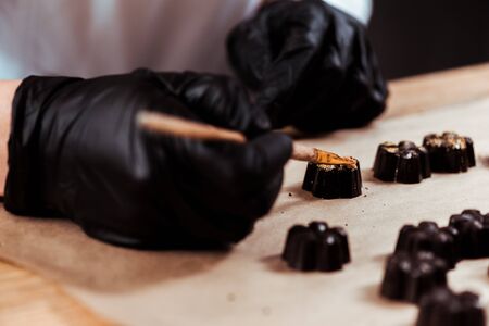 cropped view of chocolatier holding brush near prepared chocolate candiesの写真素材