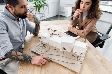 cropped view of pensive virtual reality architects looking at model of house