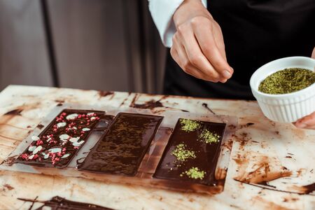 cropped view of chocolatier adding pistachio powder on dark chocolate barの写真素材