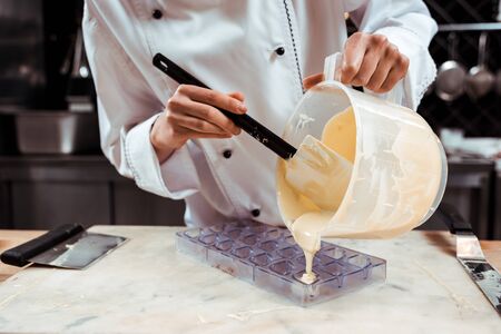 cropped view of chocolatier pouring melted white chocolate into ice trayの写真素材