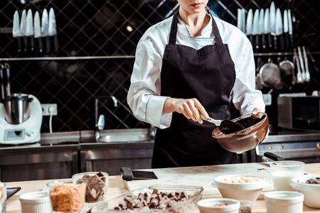 cropped view of chocolatier in apron holding silicone spatula while mixing chocolate in bowl