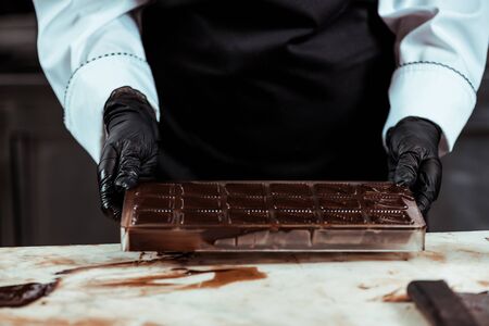cropped view of chocolatier in apron holding ice tray with melted chocolateの写真素材