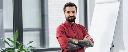 panoramic shot of handsome and smiling account manager with crossed arms looking at camera