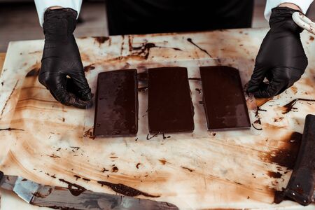 cropped view of chocolatier in latex gloves near chocolate bars