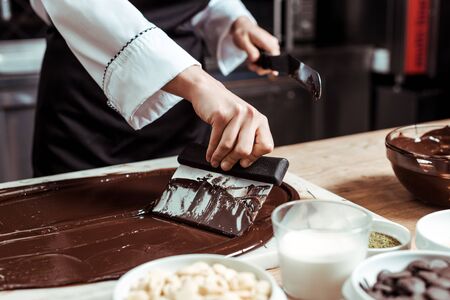 cropped view of chocolatier holding cake scraper near melted dark chocolate and milkの写真素材