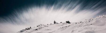 scenic view of mountain covered with snow and pine trees against dark sky in evening with white cloud, panoramic shotの写真素材
