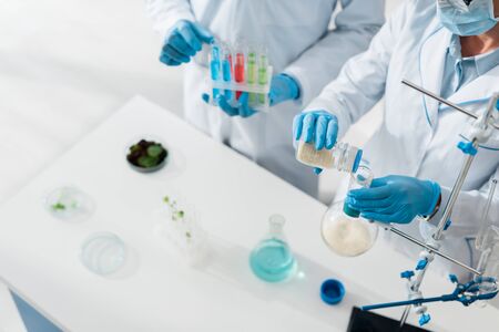 cropped view of biologists in white coats doing test in lab 