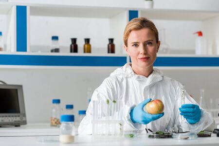 A biologist looking at camera and holding whole apple and test tube in labの写真素材