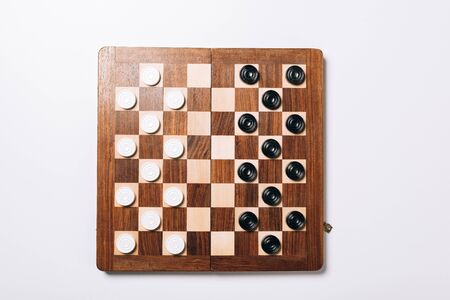 Top view of black and white checkers on wooden checkerboard on white background