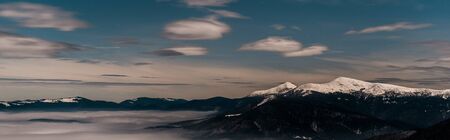 Scenic view of snowy mountains with white fluffy clouds in evening, panoramic shotの写真素材