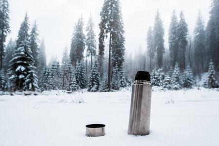Vacuum flask on snow in mountains with pine trees