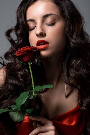 Seductive woman in red silk dress holding rose flower, isolated on greyの写真素材