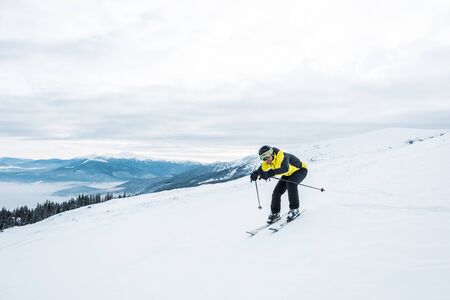 sportsman holding ski sticks and skiing on white slope in mountainsの写真素材