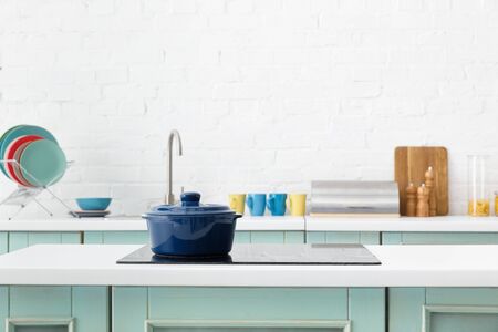 selective focus of modern white and turquoise kitchen interior with pot on electric induction cooktopの写真素材
