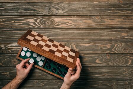 Cropped view of man taking checker from checkerboard on wooden background