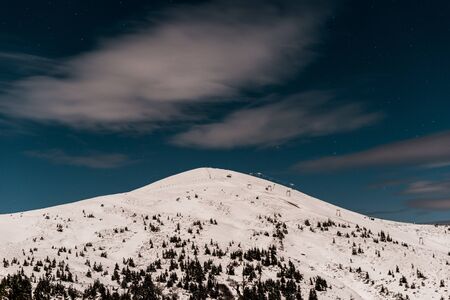 Scenic view of mountain covered with snow and pine trees against dark sky in evening