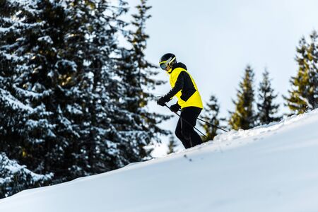 sportsman in goggles and helmet holding ski sticks while skiing near firsの写真素材