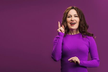 smiling woman showing idea gesture on purple backgroundの写真素材